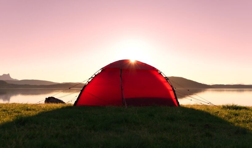 a red tent on grass by a body of water